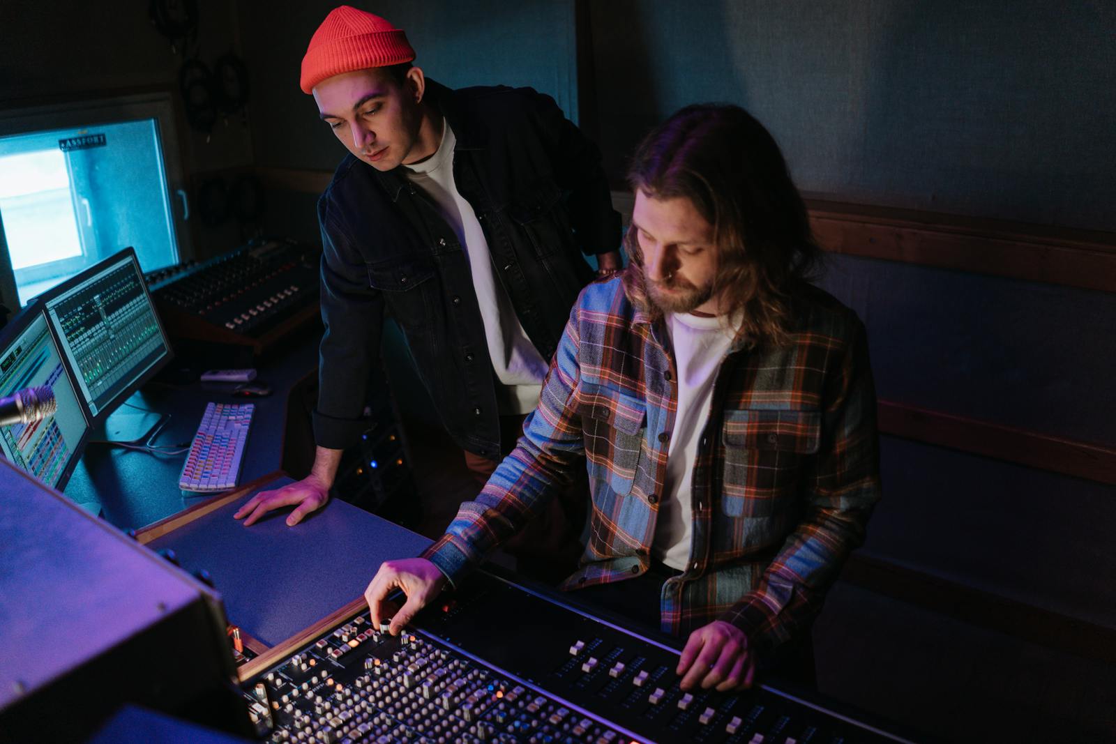 Two people leaning over a lit audio mixing board, dialling in levels, the kind of careful sound pass that separates professional audio from a clip recorded and forgotten.