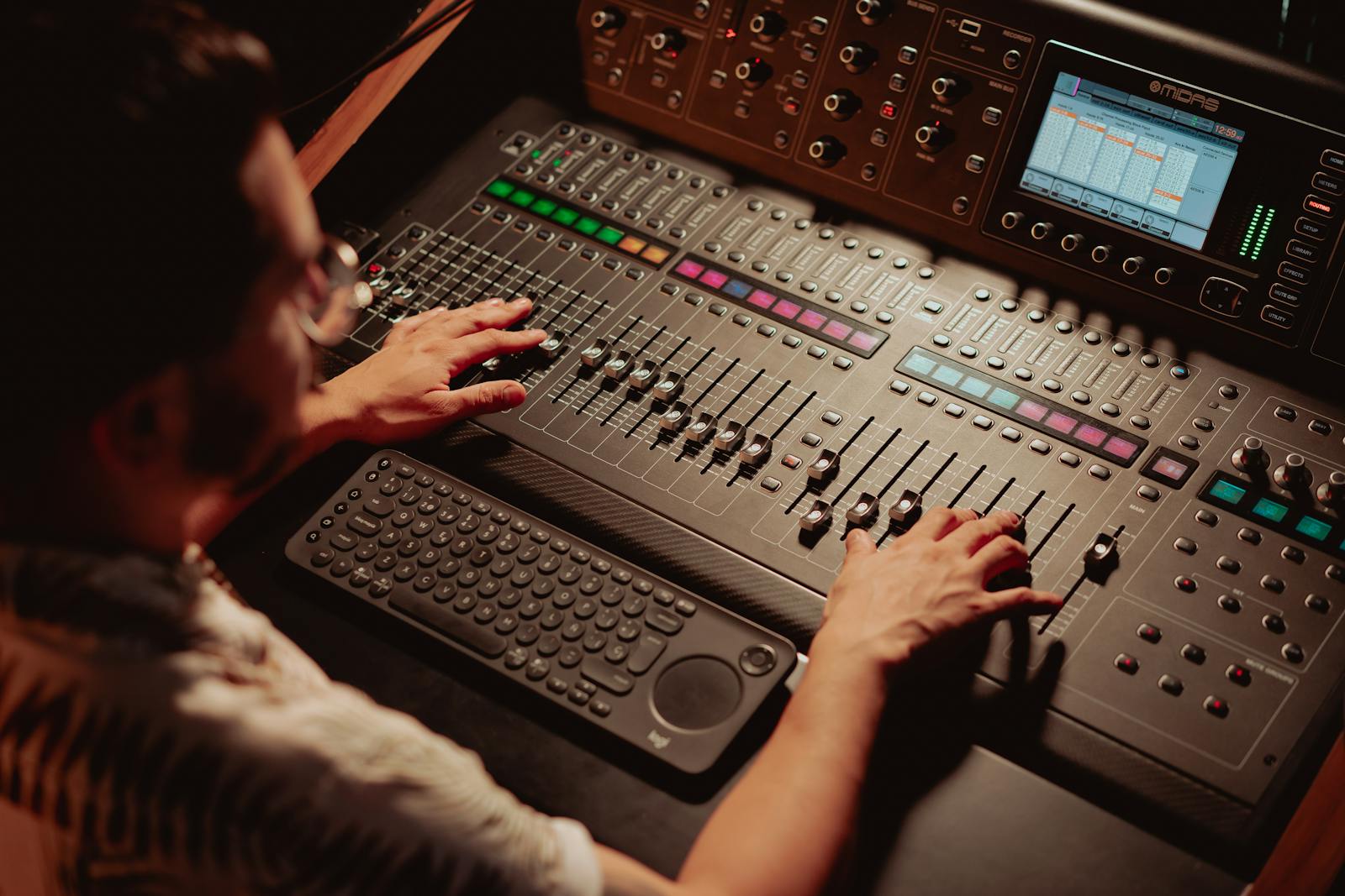 An audio engineer leaning over a mixing console with a pair of monitoring headphones, the moment where a video's voice level gets set before it is exported.