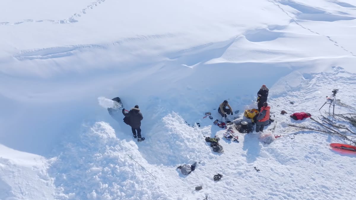 Overhead aerial of the team digging a pit into the snow to build a shelter