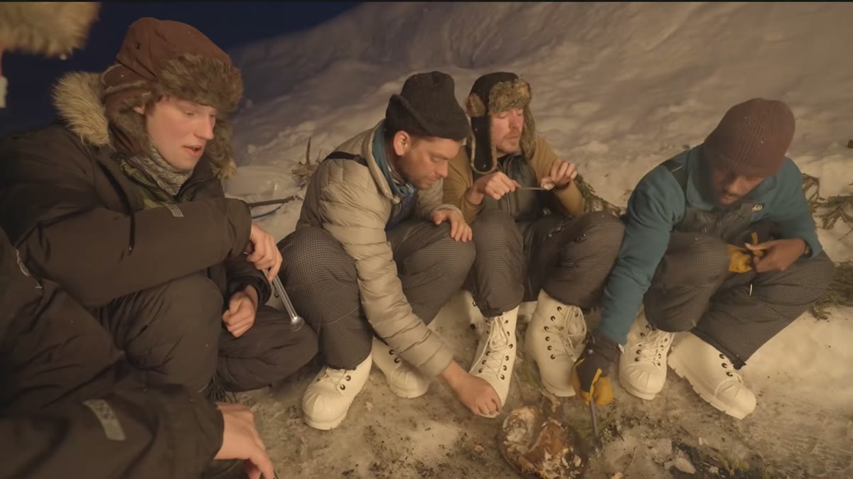 The group sitting together around a fire at dusk, warm light against the snow